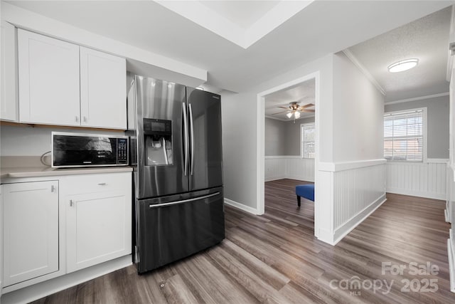 kitchen with wood finished floors, a wainscoted wall, a ceiling fan, stainless steel fridge with ice dispenser, and white cabinetry