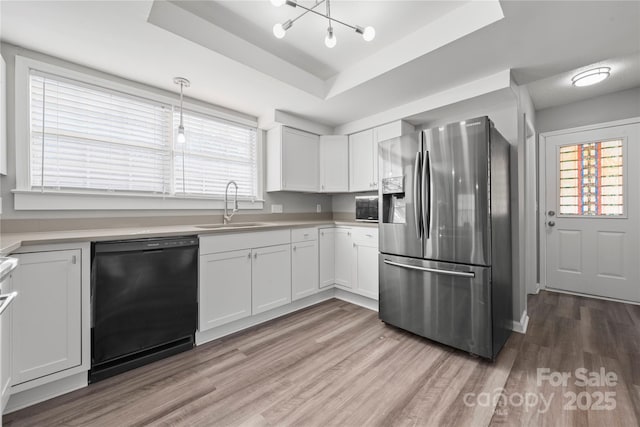 kitchen featuring a sink, black dishwasher, light wood-style floors, a raised ceiling, and stainless steel fridge