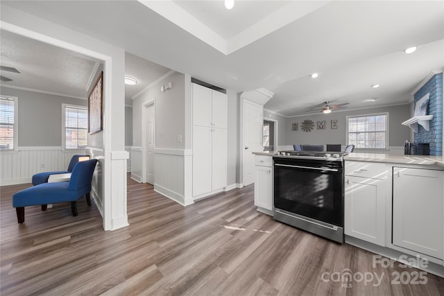 kitchen featuring ceiling fan, light countertops, ornamental molding, wainscoting, and gas stove