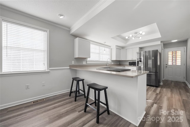 kitchen with visible vents, a kitchen breakfast bar, stainless steel fridge, a peninsula, and a raised ceiling