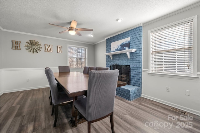 dining area with wood finished floors, visible vents, a fireplace, ornamental molding, and a textured ceiling