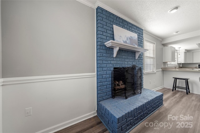 living area featuring crown molding, a brick fireplace, wood finished floors, and a textured ceiling