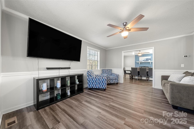 living area with visible vents, a textured ceiling, crown molding, and wood finished floors