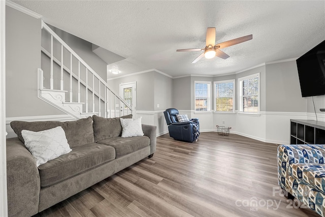 living room featuring ornamental molding, a ceiling fan, a textured ceiling, wood finished floors, and stairs