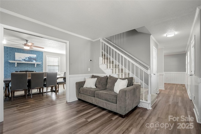 living room with ornamental molding, wood finished floors, wainscoting, and a textured ceiling