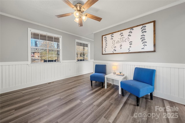 sitting room featuring visible vents, wood finished floors, a wainscoted wall, and crown molding