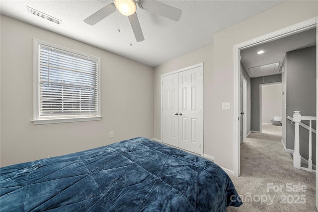 carpeted bedroom with visible vents, baseboards, attic access, a closet, and a textured ceiling