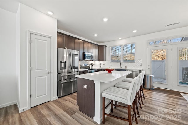 kitchen featuring a breakfast bar area, light hardwood / wood-style floors, stainless steel appliances, a kitchen island, and dark brown cabinetry