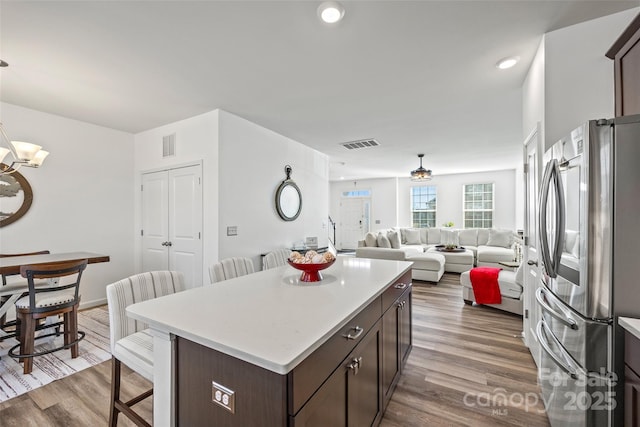 kitchen with hardwood / wood-style flooring, a breakfast bar area, stainless steel refrigerator, dark brown cabinetry, and a kitchen island