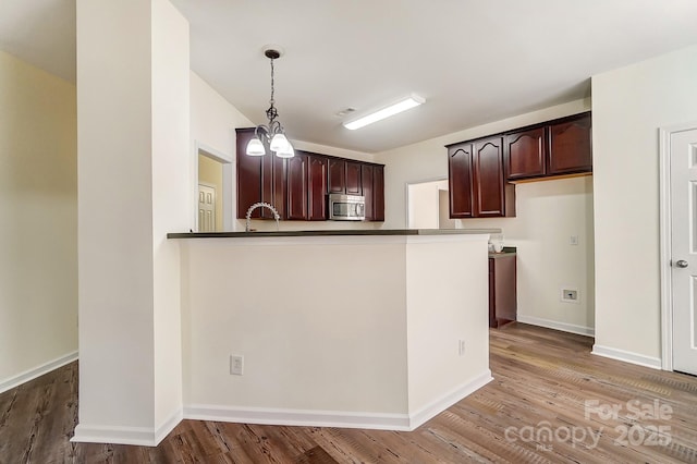 kitchen with kitchen peninsula, dark brown cabinets, pendant lighting, hardwood / wood-style flooring, and a chandelier