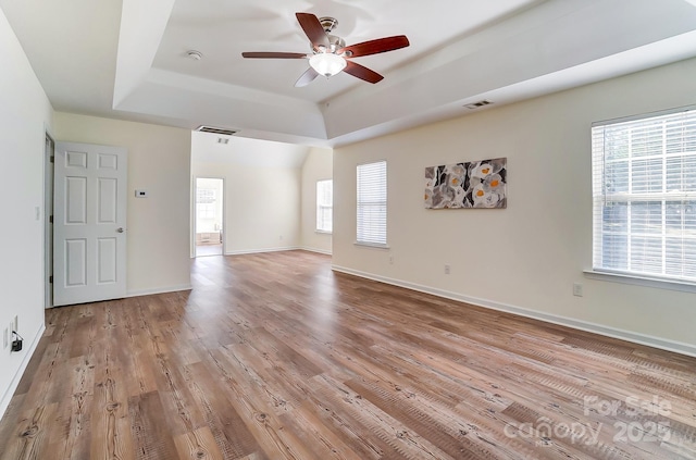 unfurnished room with a tray ceiling, ceiling fan, light hardwood / wood-style flooring, and a healthy amount of sunlight