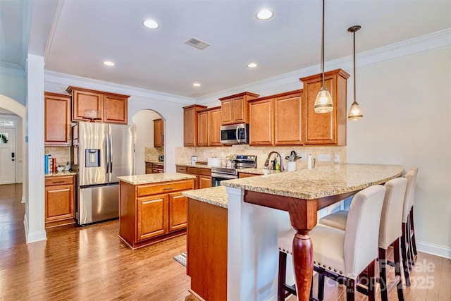 kitchen featuring pendant lighting, a breakfast bar, appliances with stainless steel finishes, light hardwood / wood-style floors, and kitchen peninsula