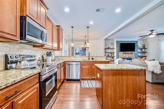 kitchen featuring a kitchen island, appliances with stainless steel finishes, sink, hanging light fixtures, and ornamental molding