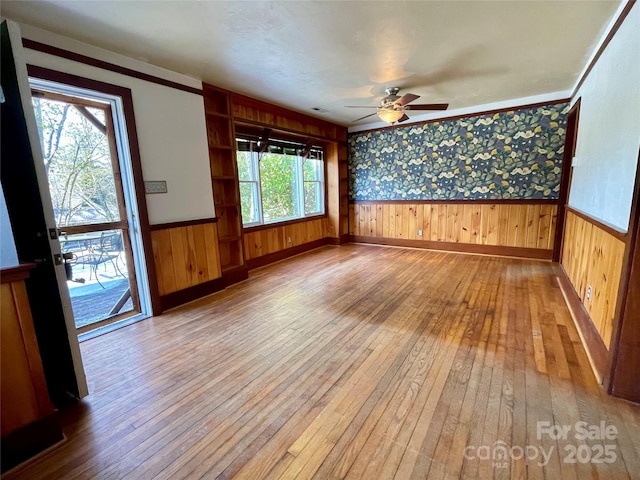 spare room with light wood-type flooring, ceiling fan, ornamental molding, and wood walls