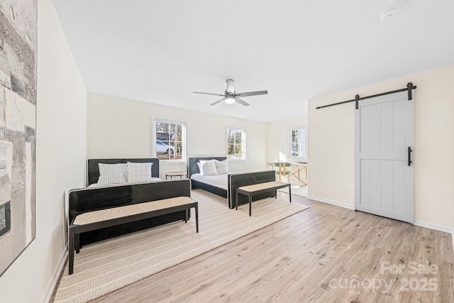 bedroom with ceiling fan, a barn door, and light hardwood / wood-style floors