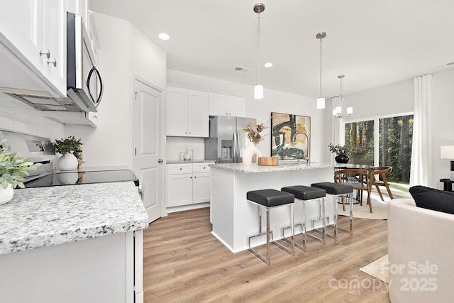 kitchen with a center island with sink, pendant lighting, white cabinetry, and appliances with stainless steel finishes