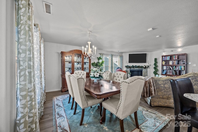 dining room featuring hardwood / wood-style floors, a stone fireplace, a textured ceiling, and an inviting chandelier