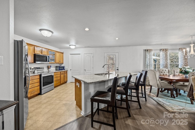 kitchen with a kitchen bar, sink, a textured ceiling, light stone counters, and stainless steel appliances