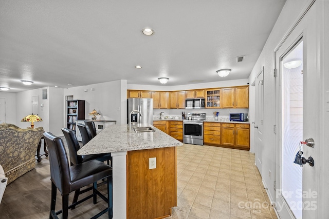 kitchen with light stone countertops, appliances with stainless steel finishes, a breakfast bar, sink, and a center island with sink