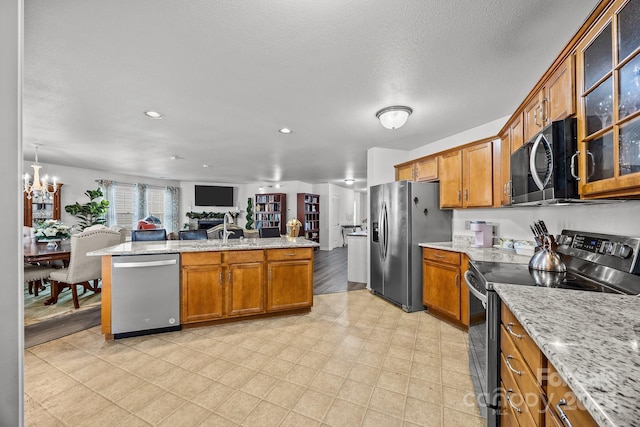 kitchen featuring appliances with stainless steel finishes, a textured ceiling, an inviting chandelier, and light stone counters