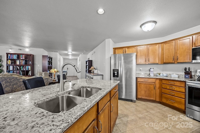 kitchen with light stone counters, sink, stainless steel appliances, and a textured ceiling