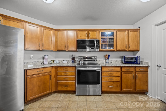 kitchen with a textured ceiling, stainless steel appliances, and light stone counters