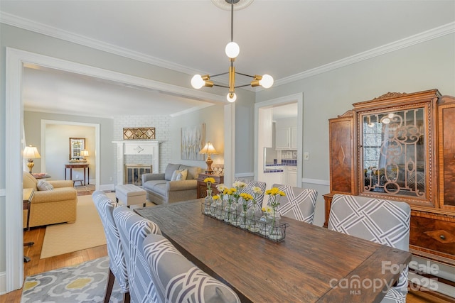 dining area featuring wood-type flooring, crown molding, a notable chandelier, and a fireplace