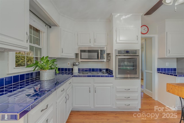 kitchen with crown molding, stainless steel appliances, tile counters, and white cabinets