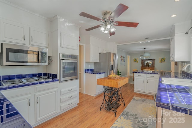 kitchen featuring sink, white cabinetry, crown molding, tile counters, and stainless steel appliances