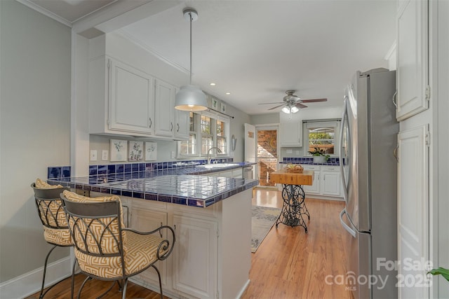 kitchen with tile countertops, stainless steel refrigerator, white cabinetry, a kitchen breakfast bar, and kitchen peninsula