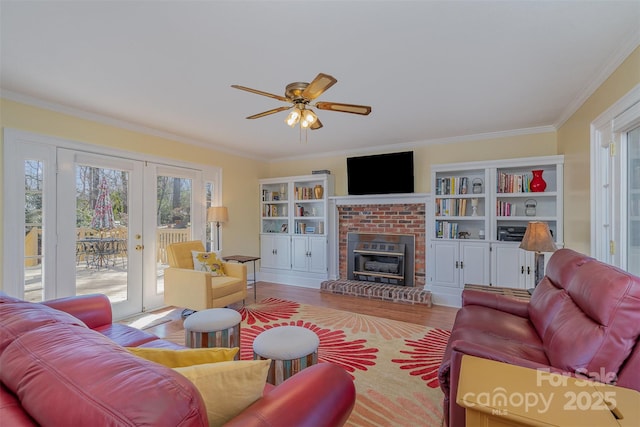 living room featuring french doors, crown molding, light wood-type flooring, ceiling fan, and a fireplace