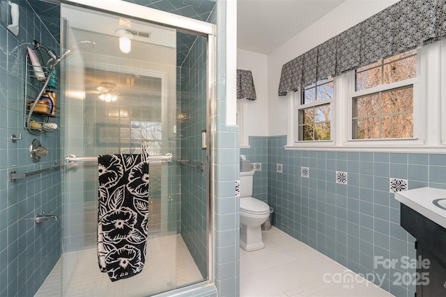 bathroom featuring a shower with door, tile walls, tile patterned flooring, vanity, and toilet