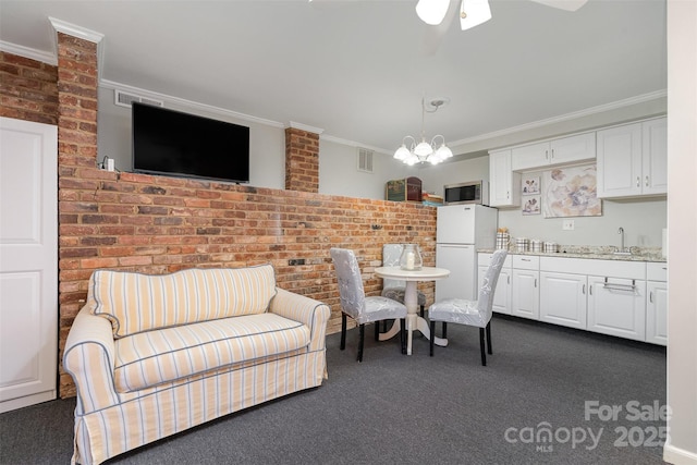 carpeted dining room with sink, crown molding, ceiling fan with notable chandelier, and brick wall