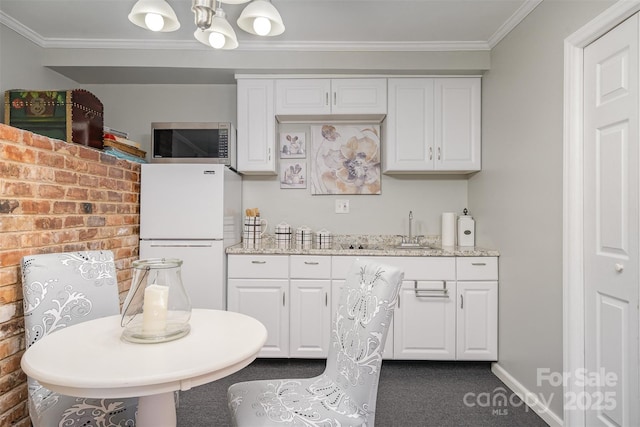 kitchen with white refrigerator, crown molding, light stone counters, and white cabinets