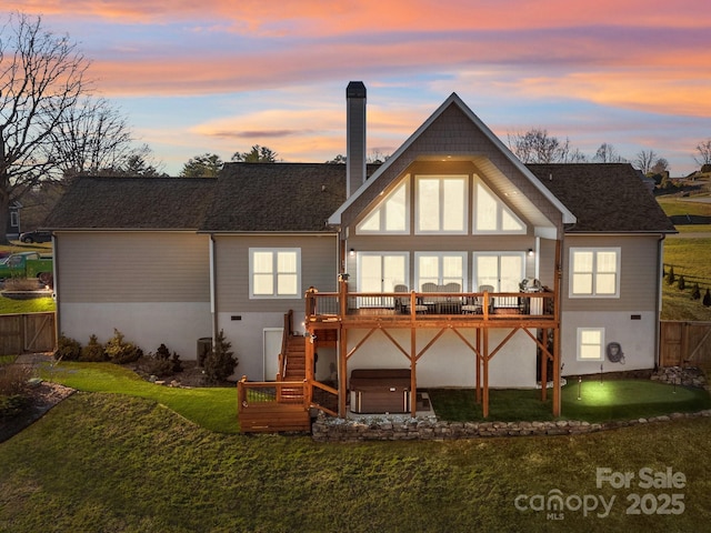 back house at dusk featuring a hot tub, a wooden deck, and a yard