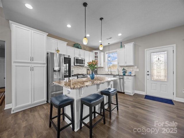 kitchen with stone counters, white cabinetry, hanging light fixtures, a center island, and stainless steel appliances