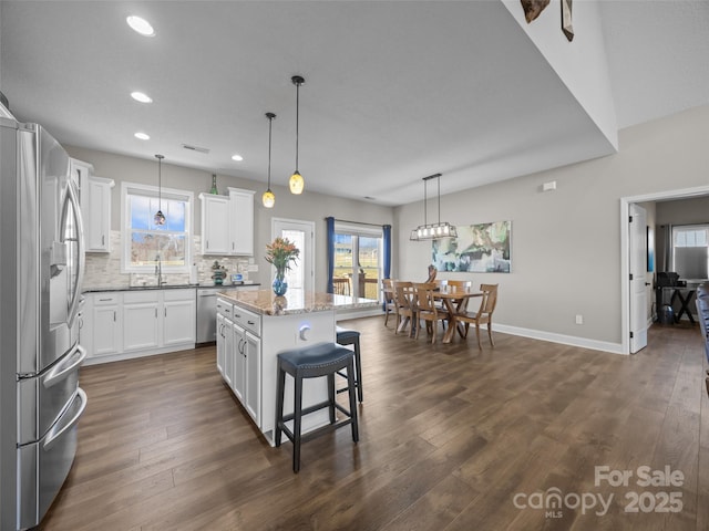 kitchen with backsplash, stainless steel appliances, a center island, white cabinets, and decorative light fixtures