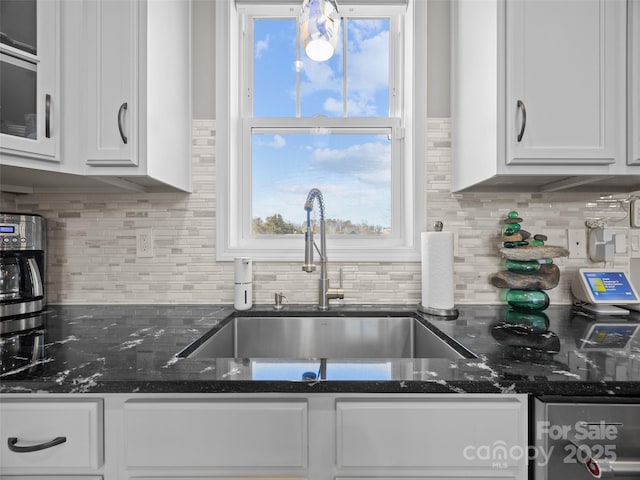 kitchen with white cabinetry, dark stone counters, sink, and backsplash