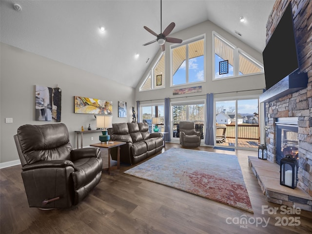 living room with ceiling fan, high vaulted ceiling, a stone fireplace, and dark hardwood / wood-style flooring