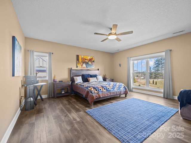 bedroom featuring multiple windows, a textured ceiling, dark hardwood / wood-style floors, and ceiling fan