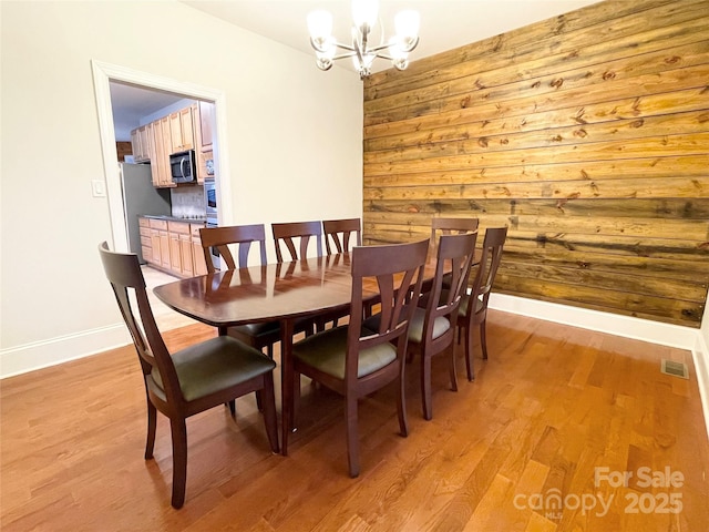 dining space with a chandelier, light hardwood / wood-style floors, and wood walls