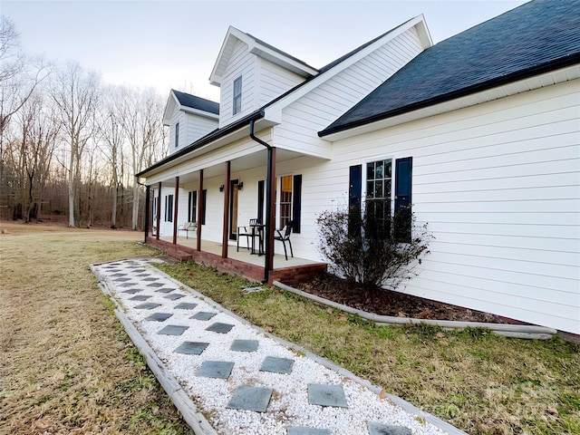 view of side of home with a porch, roof with shingles, and a lawn