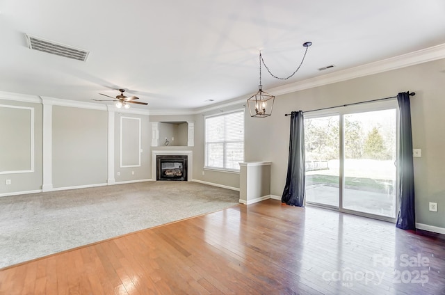 unfurnished living room with wood-type flooring, ceiling fan with notable chandelier, and ornamental molding