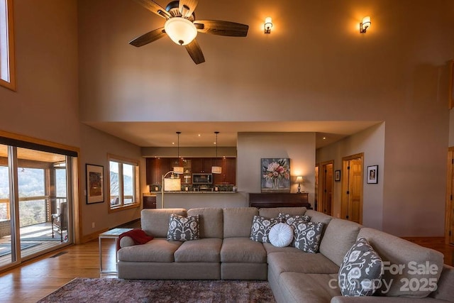 living room with ceiling fan, light hardwood / wood-style flooring, and a towering ceiling