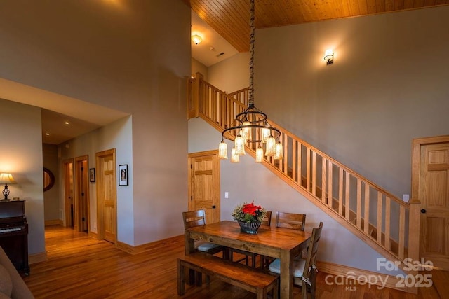 dining space with a high ceiling, wooden ceiling, a notable chandelier, and light hardwood / wood-style floors