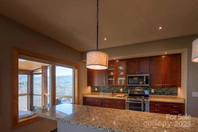 kitchen with hanging light fixtures, backsplash, light stone countertops, and appliances with stainless steel finishes