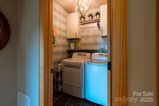 clothes washing area featuring washer and dryer, cabinets, dark tile patterned flooring, and a notable chandelier