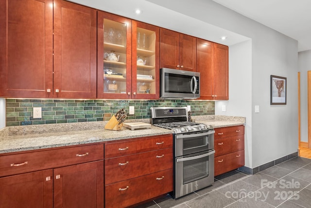 kitchen featuring light stone counters, dark tile patterned flooring, backsplash, and stainless steel appliances