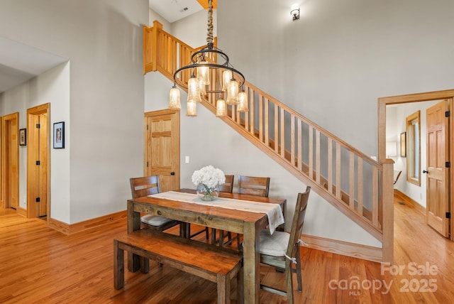 dining area with a towering ceiling, a chandelier, and light wood-type flooring