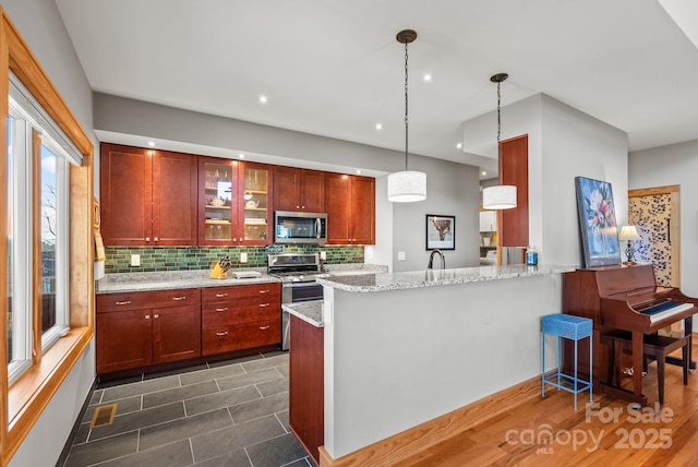 kitchen featuring light stone counters, hanging light fixtures, kitchen peninsula, stainless steel appliances, and decorative backsplash